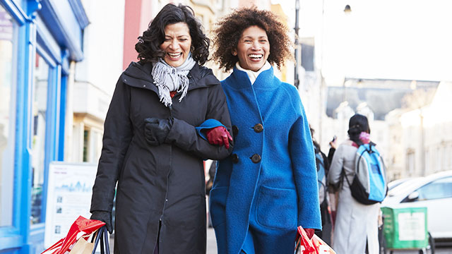 Two middle aged women smiling while walking in a sidewalk with shopping bags